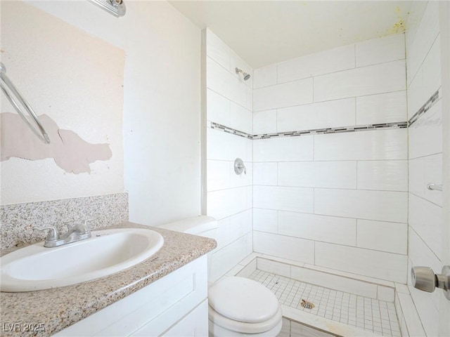 bathroom with toilet, a tile shower, and vanity