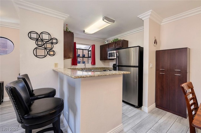 kitchen featuring kitchen peninsula, a breakfast bar area, appliances with stainless steel finishes, light stone countertops, and crown molding