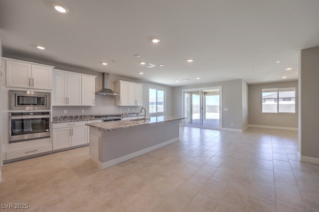 kitchen featuring wall chimney range hood, a center island with sink, sink, white cabinetry, and stainless steel appliances