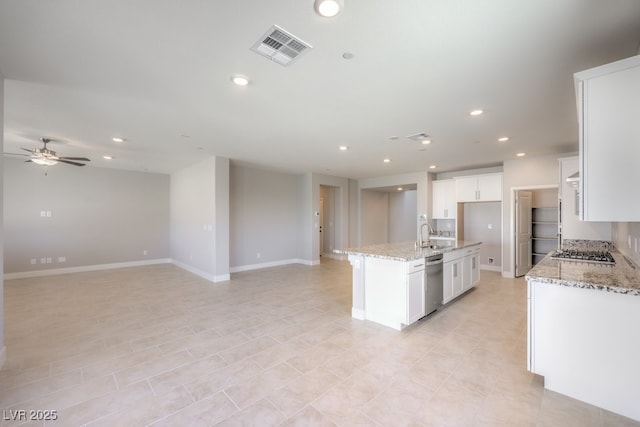 kitchen with white cabinetry, ceiling fan, appliances with stainless steel finishes, a kitchen island with sink, and light stone countertops