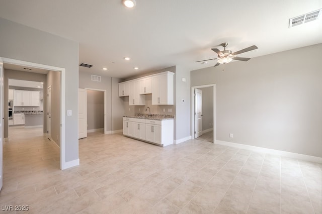 kitchen featuring light tile patterned floors, ceiling fan, white cabinets, light stone counters, and sink