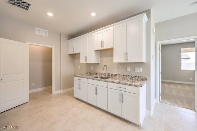 kitchen featuring white cabinetry, light stone counters, and sink