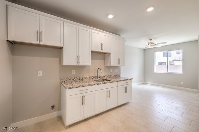 kitchen with light stone countertops, ceiling fan, white cabinetry, and sink