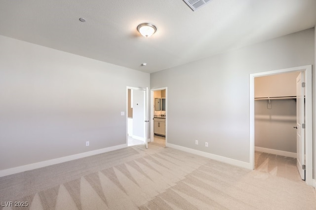 unfurnished bedroom featuring connected bathroom, light carpet, a closet, and a walk in closet