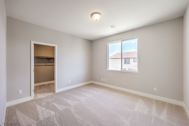 unfurnished bedroom with a spacious closet, a closet, and light colored carpet