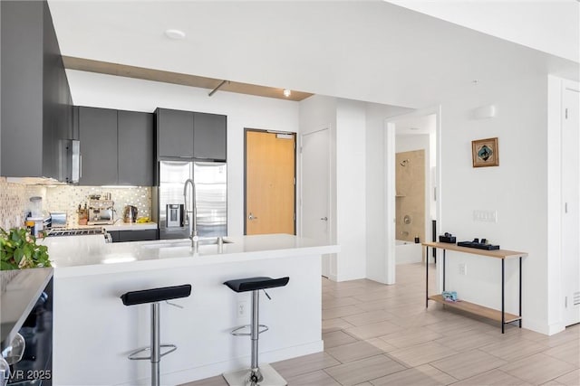 kitchen with a kitchen bar, sink, stainless steel fridge, gray cabinets, and kitchen peninsula