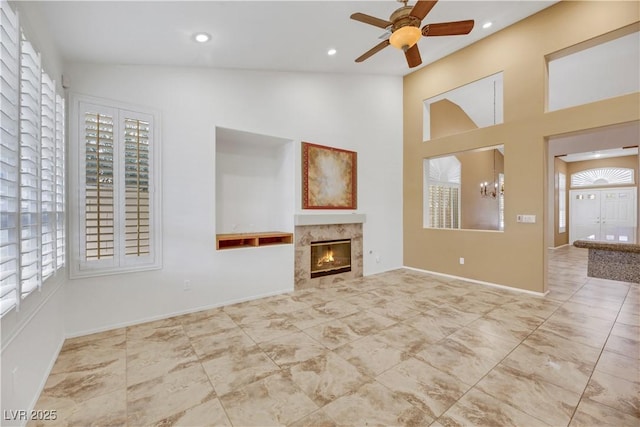 unfurnished living room with vaulted ceiling, a high end fireplace, and ceiling fan with notable chandelier