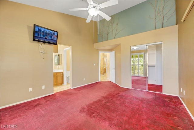 unfurnished bedroom featuring a towering ceiling, carpet floors, a closet, ceiling fan, and ensuite bathroom