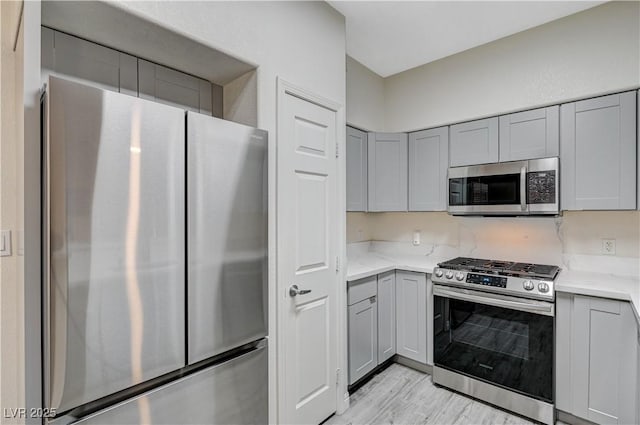 kitchen featuring light stone counters, appliances with stainless steel finishes, light wood-type flooring, and gray cabinetry