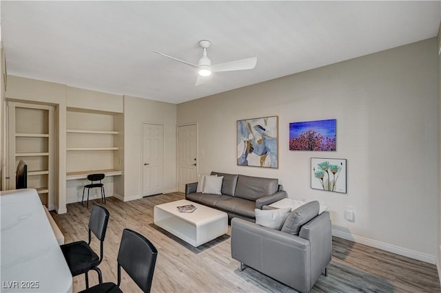 living room featuring built in features, built in desk, light hardwood / wood-style floors, and ceiling fan