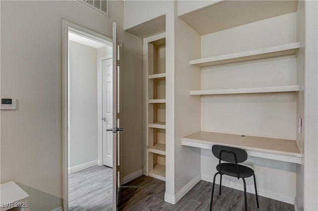 unfurnished office featuring dark hardwood / wood-style flooring and built in desk