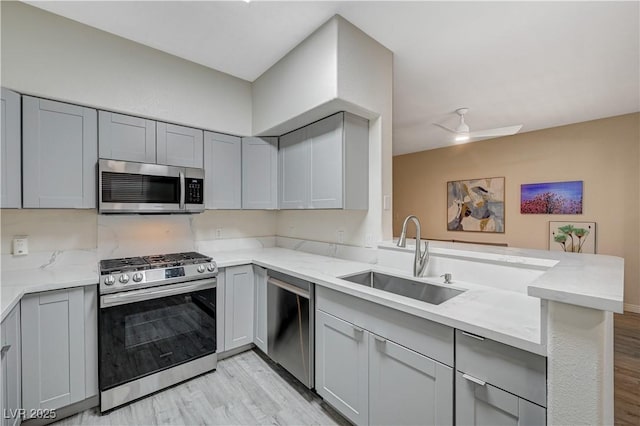 kitchen with appliances with stainless steel finishes, kitchen peninsula, sink, and gray cabinetry