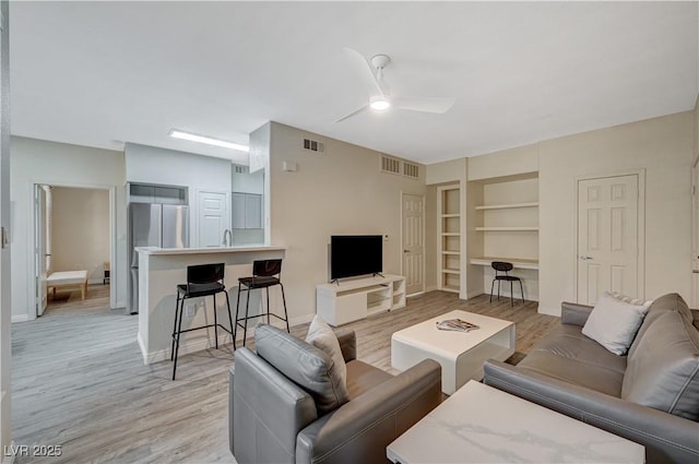 living room with ceiling fan, sink, light hardwood / wood-style floors, and built in shelves