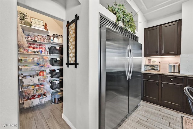 kitchen featuring built in fridge, light stone countertops, backsplash, dark brown cabinets, and a barn door