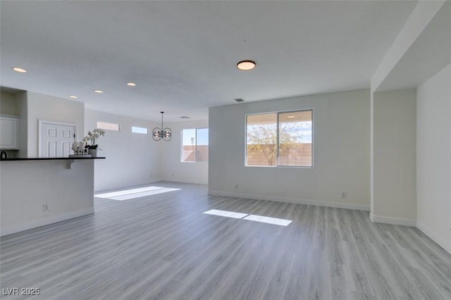 unfurnished living room featuring an inviting chandelier and light hardwood / wood-style flooring