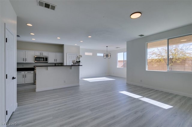 kitchen featuring a healthy amount of sunlight, decorative light fixtures, light wood-type flooring, a chandelier, and white cabinets