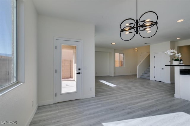 interior space featuring light wood-type flooring, a chandelier, pendant lighting, and white cabinetry