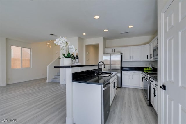 kitchen featuring a center island with sink, sink, white cabinetry, light wood-type flooring, and stainless steel appliances