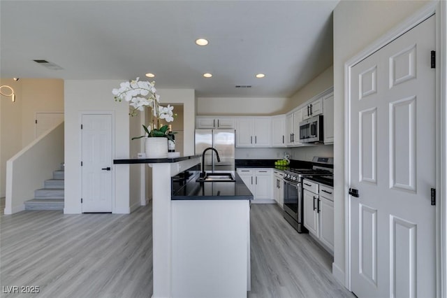 kitchen with decorative light fixtures, sink, white cabinetry, light wood-type flooring, and stainless steel appliances