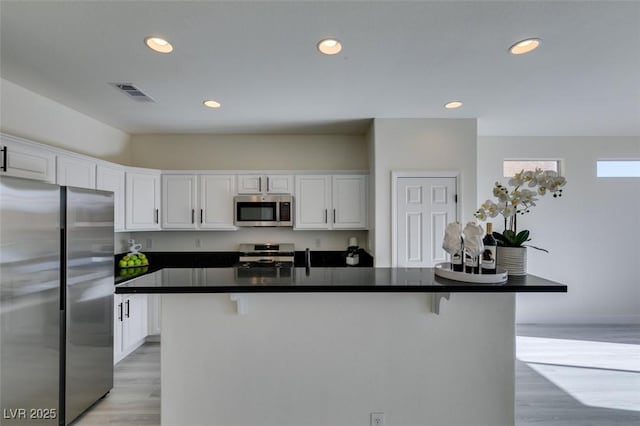 kitchen featuring a kitchen bar, white cabinetry, light hardwood / wood-style flooring, appliances with stainless steel finishes, and an island with sink