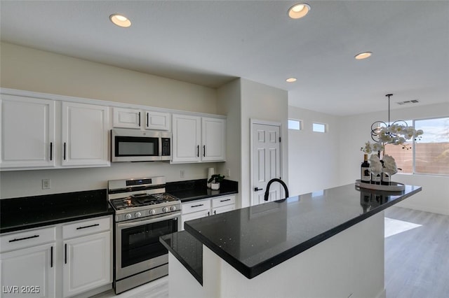 kitchen with appliances with stainless steel finishes, a center island, white cabinetry, hanging light fixtures, and a chandelier