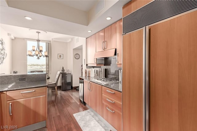 kitchen featuring decorative light fixtures, stainless steel gas stovetop, dark stone countertops, a notable chandelier, and paneled fridge