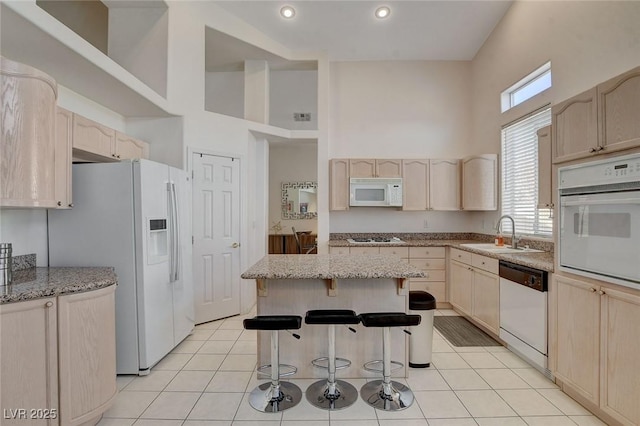 kitchen with white appliances, a center island, light brown cabinets, sink, and light tile patterned floors