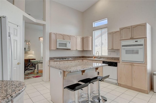 kitchen with sink, white appliances, a center island, a high ceiling, and light brown cabinetry