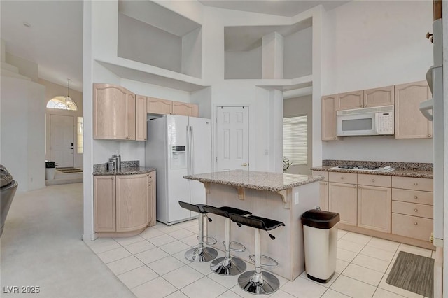 kitchen featuring a breakfast bar, white appliances, light brown cabinetry, and light tile patterned floors