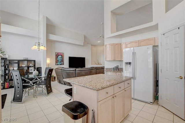 kitchen featuring light brown cabinetry, white refrigerator with ice dispenser, hanging light fixtures, light tile patterned flooring, and a kitchen island