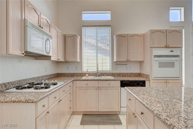 kitchen featuring light stone countertops, white appliances, light brown cabinetry, sink, and light tile patterned flooring