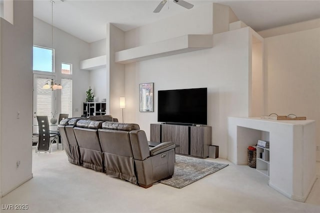 carpeted living room featuring ceiling fan with notable chandelier and a high ceiling