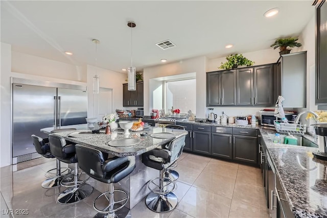 kitchen featuring sink, a kitchen island, dark stone counters, and stainless steel built in refrigerator