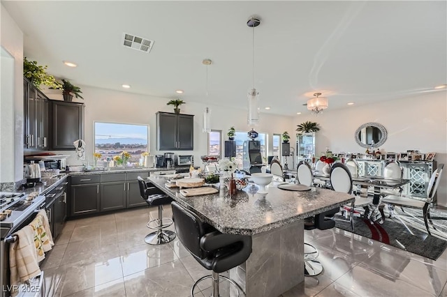 kitchen with a center island, a kitchen bar, decorative light fixtures, dark stone countertops, and stainless steel gas range oven