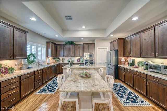 kitchen featuring a breakfast bar, dark brown cabinets, stainless steel appliances, a center island, and light stone countertops