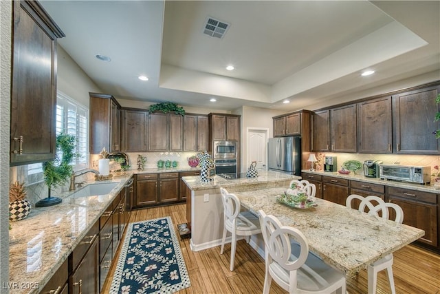 kitchen featuring stainless steel appliances, a sink, visible vents, a raised ceiling, and a kitchen bar