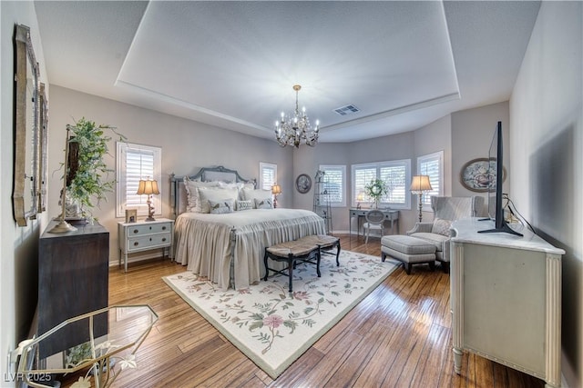 bedroom with a raised ceiling, an inviting chandelier, and light hardwood / wood-style flooring