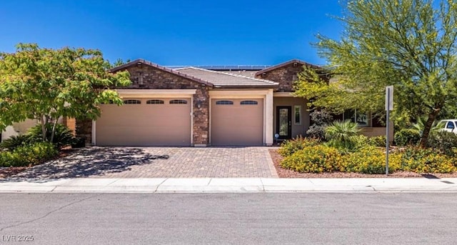 view of front of house with a garage, solar panels, stone siding, a tiled roof, and decorative driveway