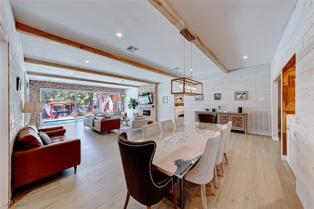 dining space with light hardwood / wood-style flooring, beam ceiling, a notable chandelier, and a fireplace