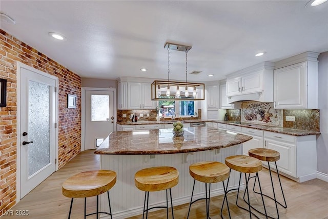 kitchen with brick wall, pendant lighting, a kitchen island, and light stone countertops