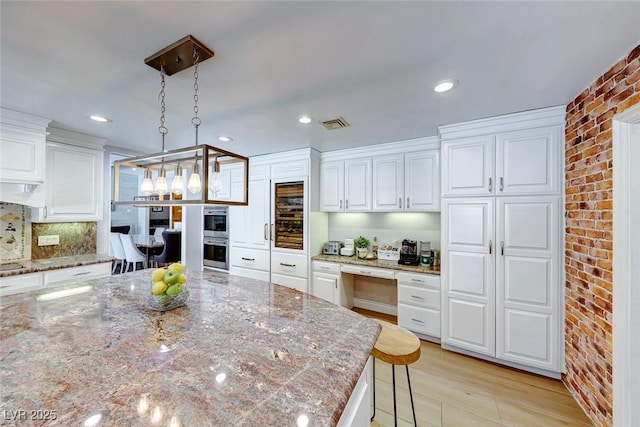 kitchen with light stone countertops, a kitchen breakfast bar, hanging light fixtures, and white cabinets