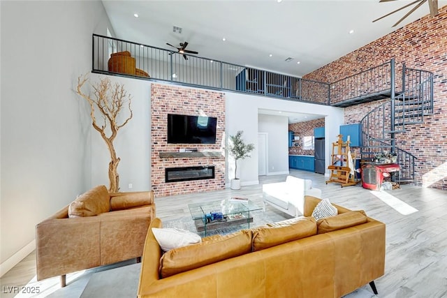 living room with a high ceiling, brick wall, a fireplace, light wood-type flooring, and ceiling fan