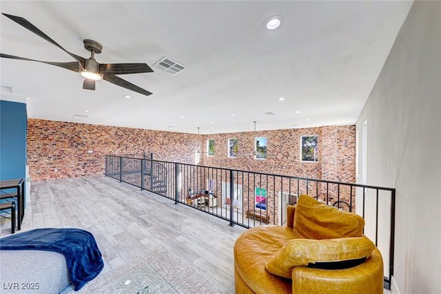 living area with ceiling fan, brick wall, and light hardwood / wood-style flooring