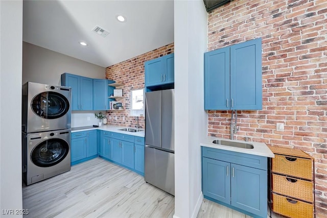 kitchen featuring stacked washer and clothes dryer, blue cabinets, stainless steel fridge, and sink