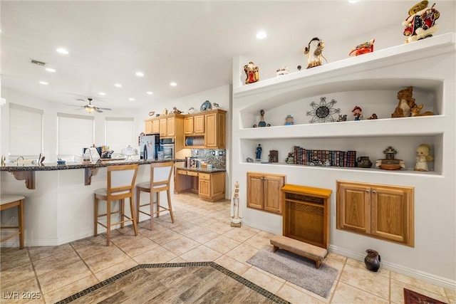 kitchen featuring a breakfast bar area, appliances with stainless steel finishes, ceiling fan, tasteful backsplash, and light tile patterned flooring