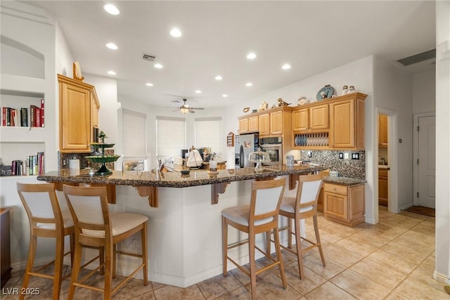 kitchen with stainless steel appliances, dark stone counters, backsplash, kitchen peninsula, and ceiling fan