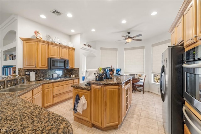 kitchen featuring appliances with stainless steel finishes, a kitchen island, dark stone counters, sink, and backsplash