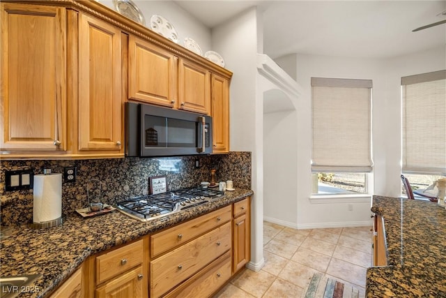 kitchen with dark stone countertops, backsplash, stainless steel gas cooktop, ceiling fan, and light tile patterned floors