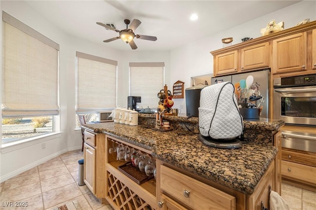 kitchen featuring a kitchen island, dark stone countertops, oven, ceiling fan, and light tile patterned floors