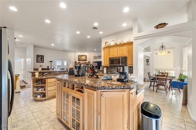 kitchen with a center island, light brown cabinets, dark stone counters, stainless steel refrigerator, and light tile patterned floors